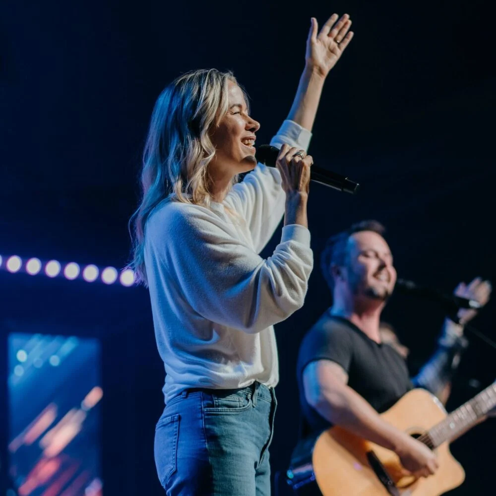 A worship leader singing with one hand raised beside a guitarist